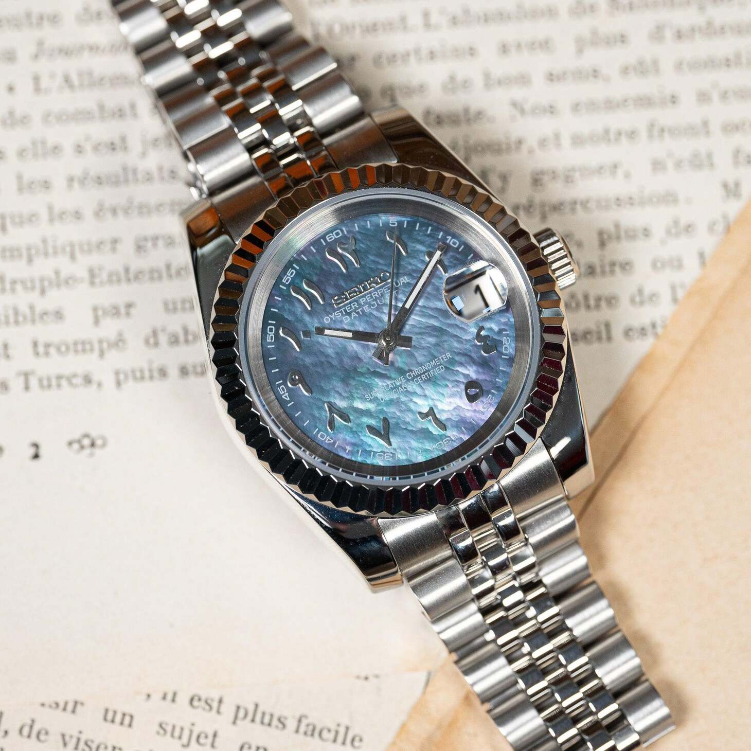 Top view of Seiko Mod Datejust Cosmos Arabic with blue mother of pearl dial on open book background