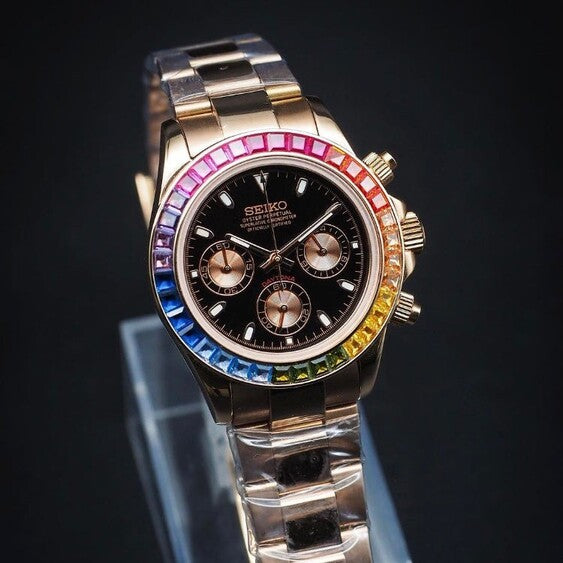 Frontal view of the Seiko Mod Daytona Rose Gold Rainbow on a display stand, showing the full watch with its rainbow bezel, rose gold bracelet, and black dial.