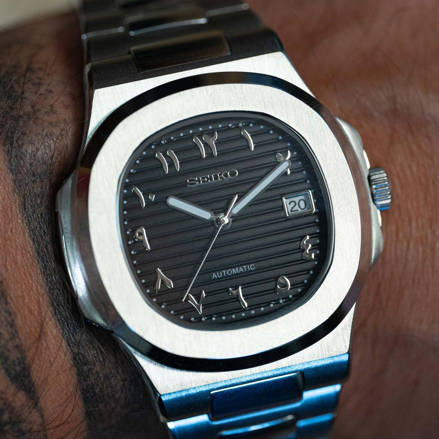 Wrist shot of Seiko mod Nautilus black Arabic dial reflecting light on brushed steel case