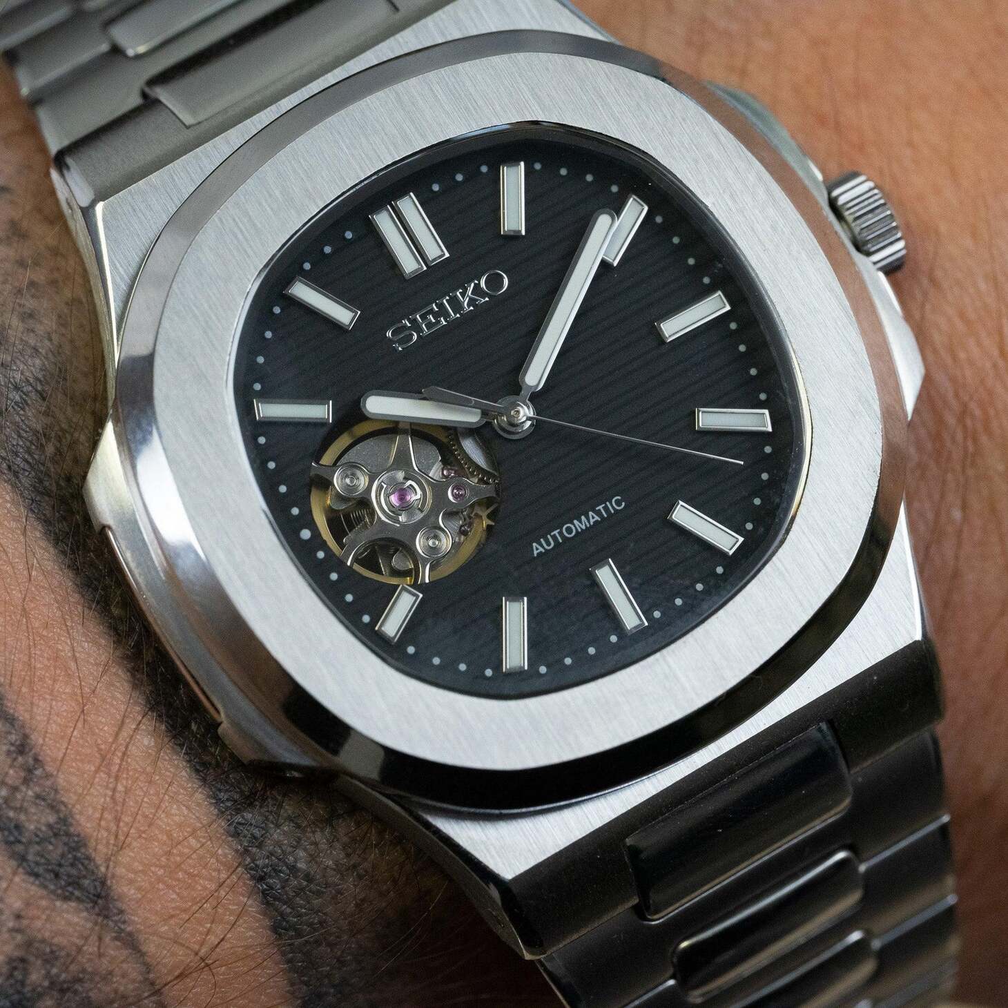 Wrist view of Seiko mod Nautilus black open heart reflecting light on brushed steel finish