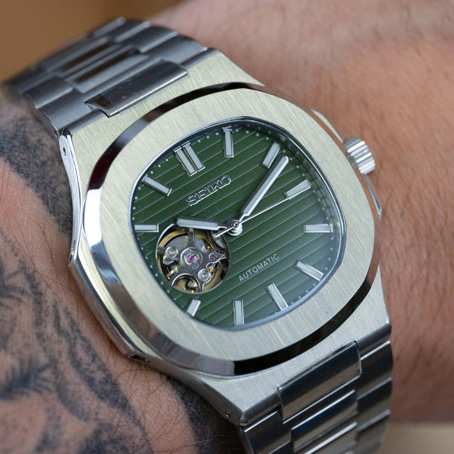 Wrist view of Seiko mod Nautilus olive green open heart watch with brushed steel bracelet
