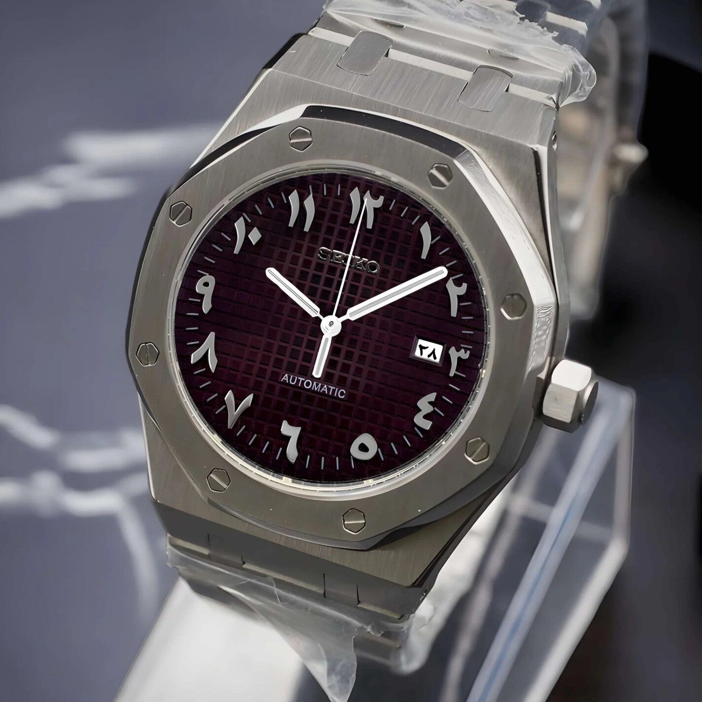 Right angled close up of the Seiko Mod Royal Oak with brushed stainless steel case, deep brown textured dial featuring Arabic numerals and a date window at three o’clock.