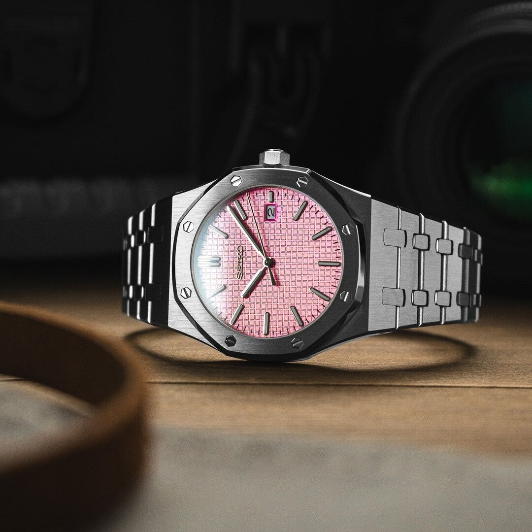 horizontal view of Seiko Mod Royal Oak watch showcasing a striking pink textured dial with silver baton markers, set in a brushed stainless steel octagonal case and complemented by an integrated steel bracelet.