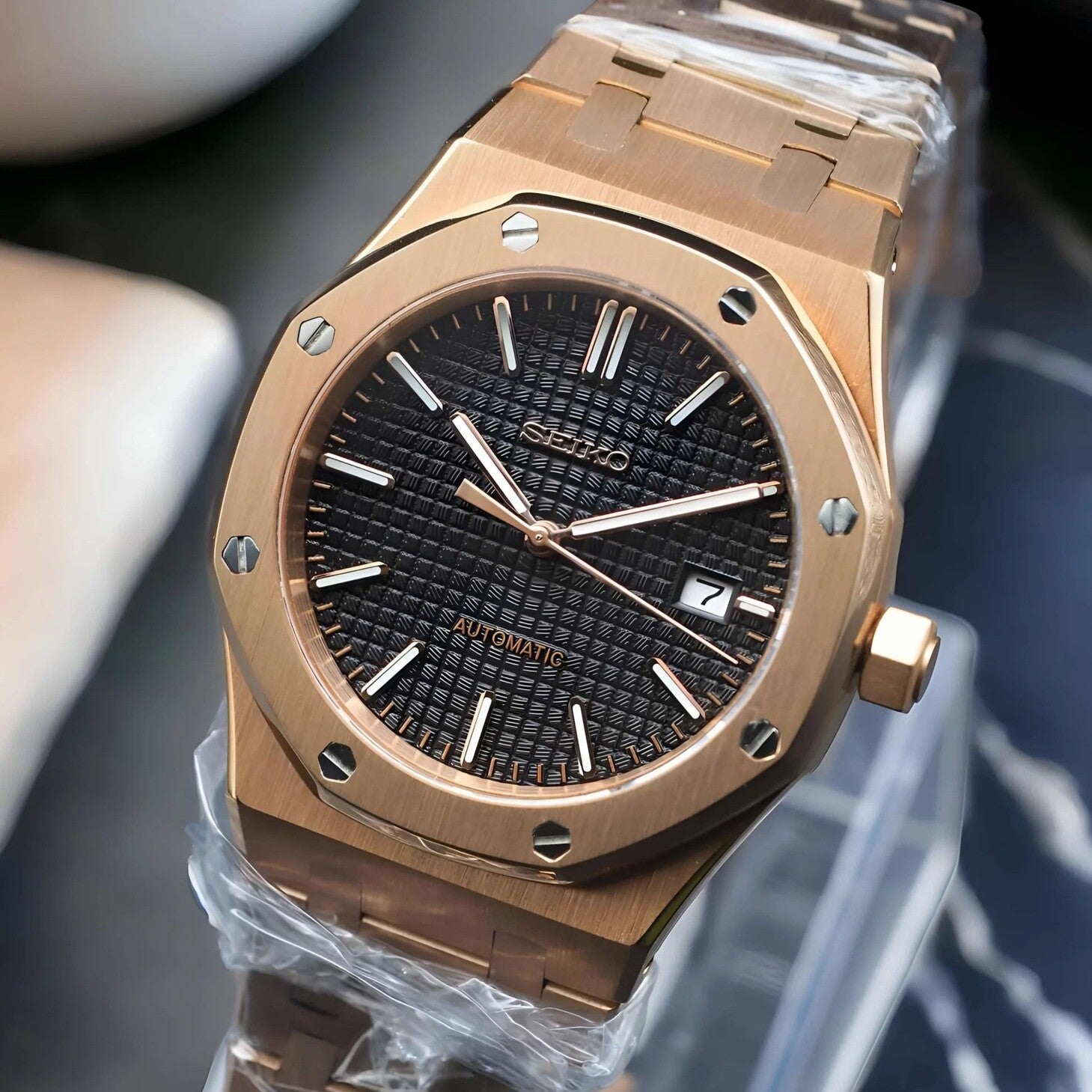 Right angled view of Seiko Mod Royal Oak in rose gold, showing the brushed case, black textured dial with date display, and polished bezel screws, highlighting the elegance of the overall design.
