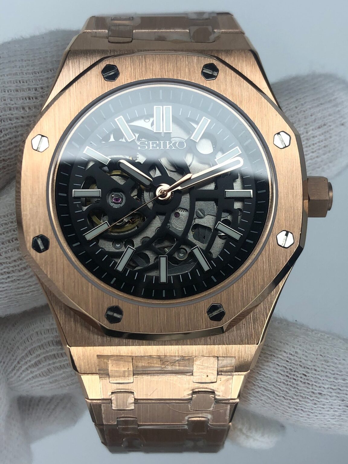 Close up front view of the Seiko Mod Royal Oak in rose gold finish, showcasing a brushed octagonal bezel with black screws, skeletonized dial revealing the mechanical movement beneath, luminous indices, and a matching integrated rose gold bracelet.