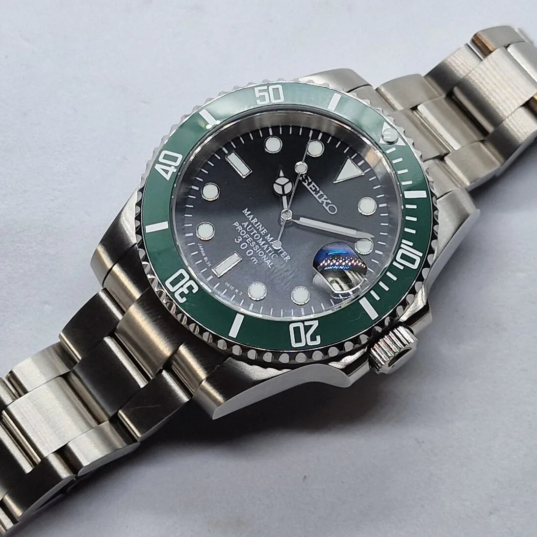 Seiko Mod Submariner Kermit mit gruener Luenette, schwarzem Zifferblatt und Edelstahlarmband – automatische Taucheruhr im klassischen Submariner-Stil.