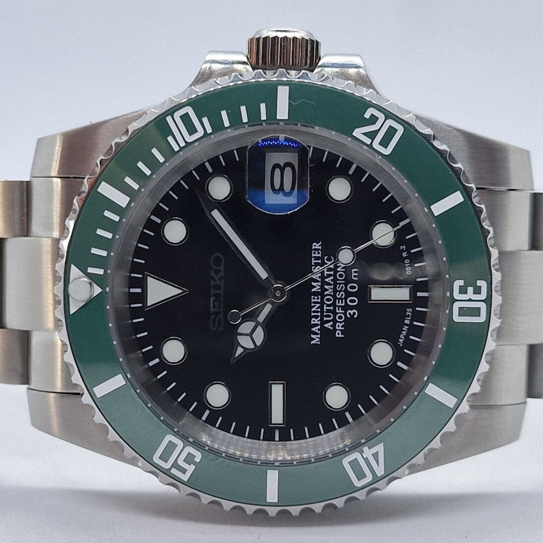 Nahaufnahme der Seiko Mod Submariner Kermit mit schwarzem Zifferblatt, gruener Luenette und Edelstahlarmband – automatische Taucheruhr inspiriert vom Rolex Submariner Design.