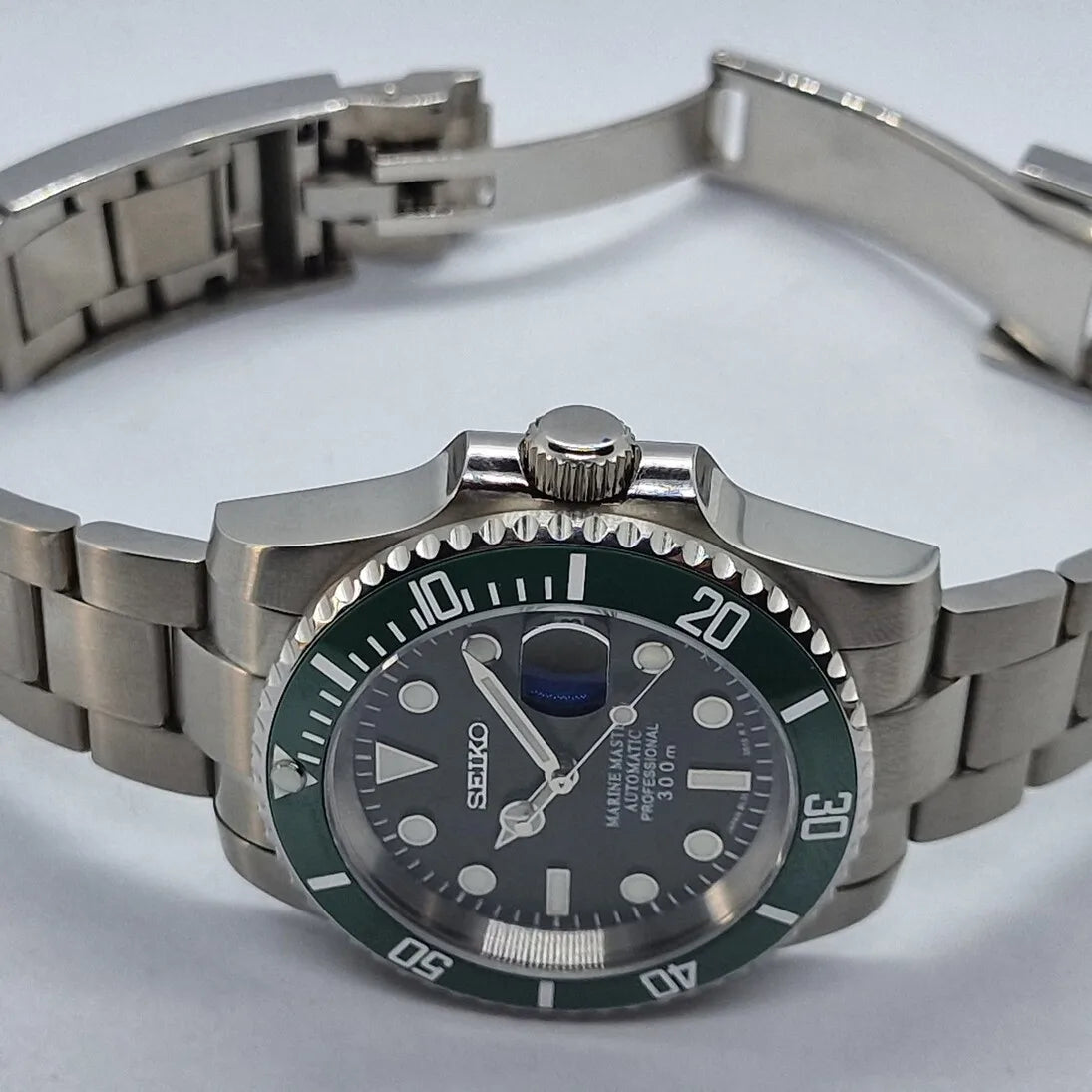 Seitenansicht der Seiko Mod Submariner Kermit mit geoeffnetem Edelstahlarmband, gruener Luenette und schwarzem Zifferblatt. Das Foto hebt die verschraubte Krone und das massive Gehaeuse der automatischen Taucheruhr hervor.