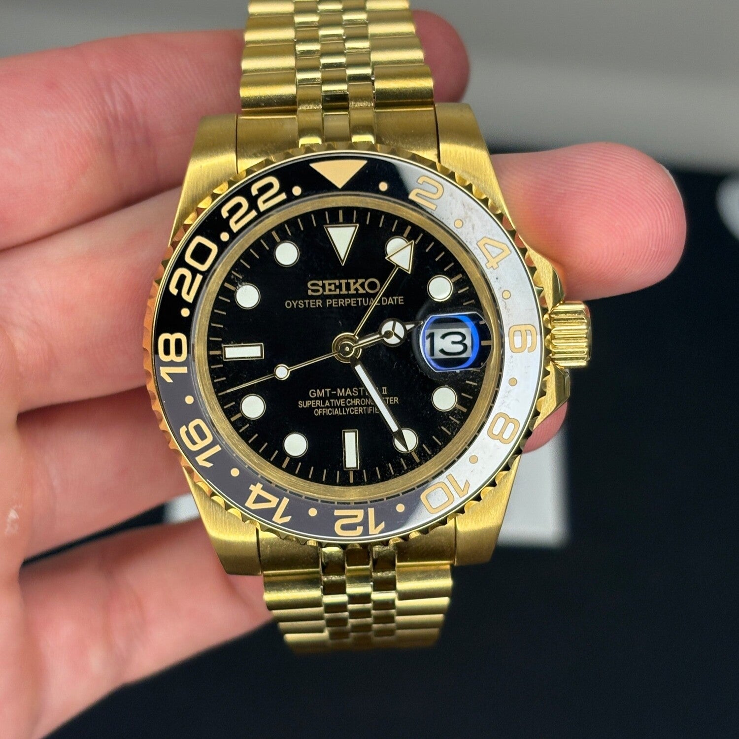 GMT Gold Frontansicht, schwarzes Zifferblatt, goldene Leuchtindizes, Cyclops Datumslupe, goldene Lünette, NH34 GMT Automatikuhr