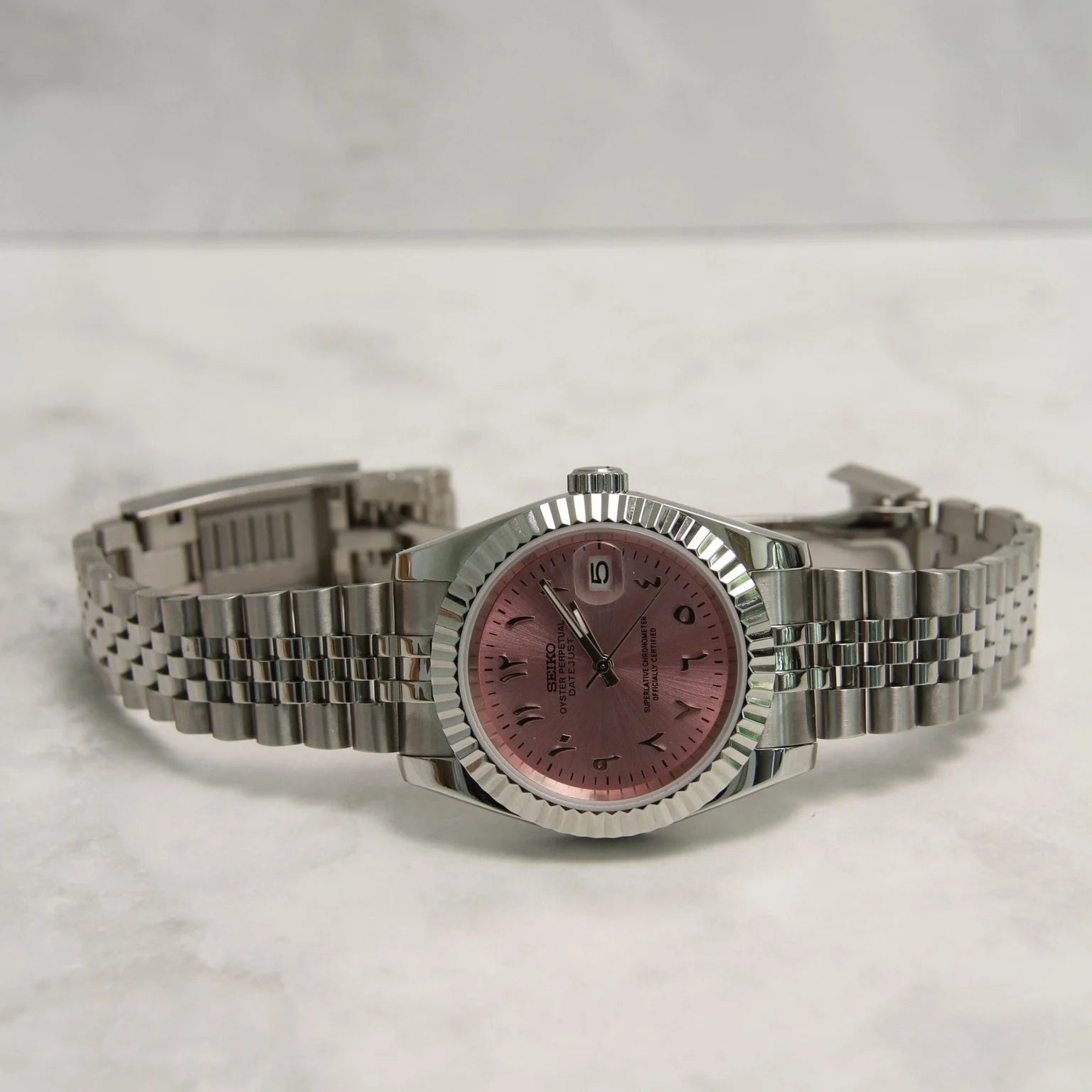 Seiko Mod Datejust Rose Arabic Luxusuhr mit rosa Zifferblatt, arabischen Ziffern, Saphirglas, NH35 Automatikwerk und Edelstahlarmband auf Marmor-Hintergrund