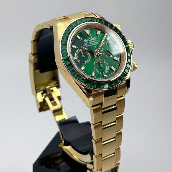 Seiko Mod Daytona Green Emerald Herrenuhr Schrägansicht mit vergoldetem Oyster-Armband, Smaragd-Lünette, Green Emerald Sonnenschliff-Zifferblatt, Chronograph-Drückern und VK63 Uhrwerk