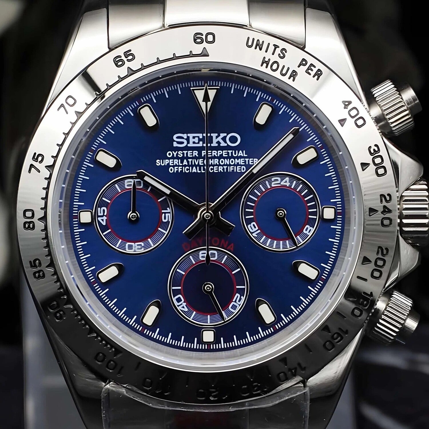 Nahaufnahme der Seiko Mod Daytona Royal Blue Metallic mit metallischem Royal Blue Zifferblatt, silbernen Totalisatoren, roten Akzenten, VK63 Chronograph-Funktion, Edelstahl-Tachymeter-Lünette und Kronendetail