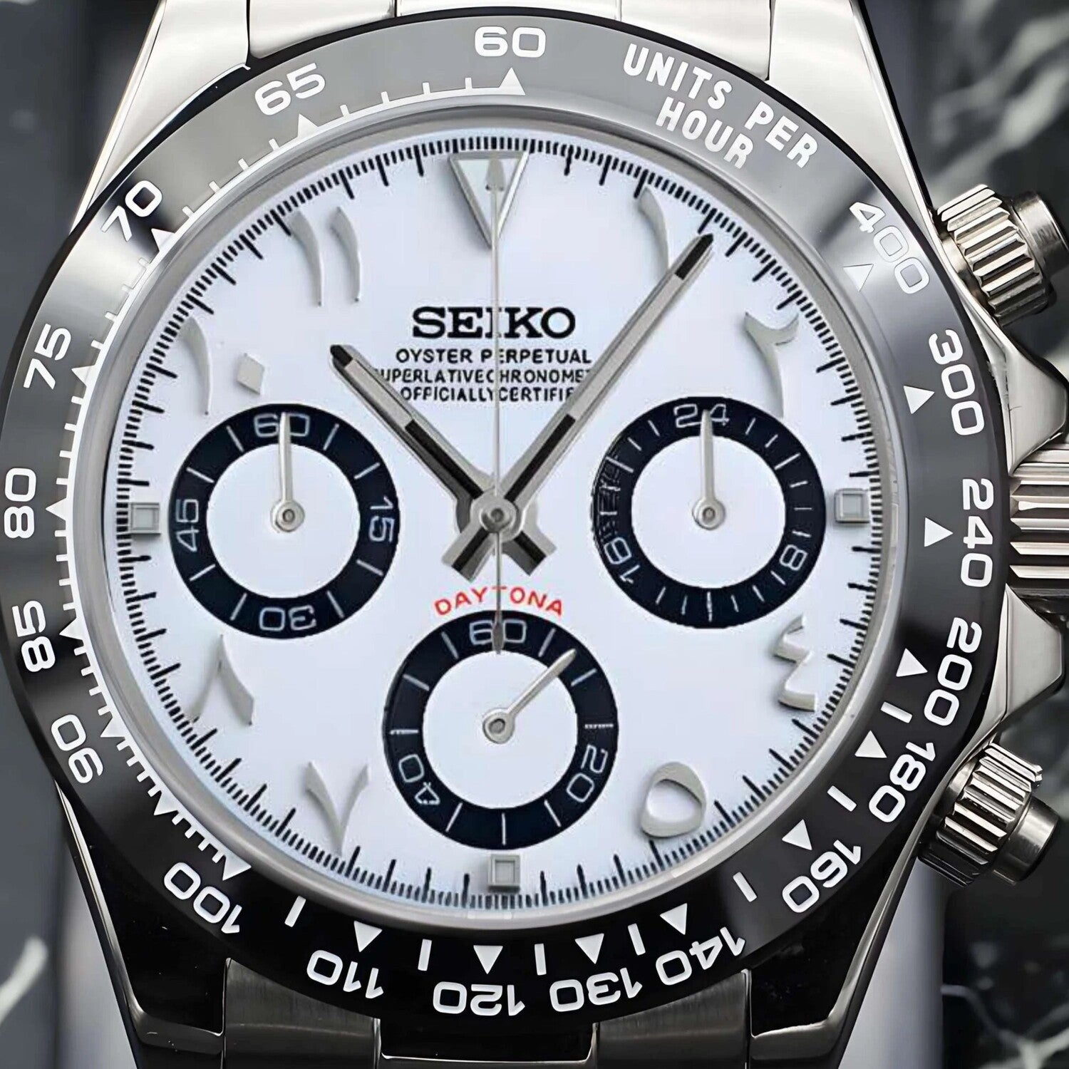 Nahaufnahme der Seiko Mod Daytona White Arabic mit weißem Zifferblatt, arabischen Ziffern, drei schwarzen Totalisatoren, VK63 Chronograph-Funktion und schwarzer Keramik-Tachymeter-Lünette