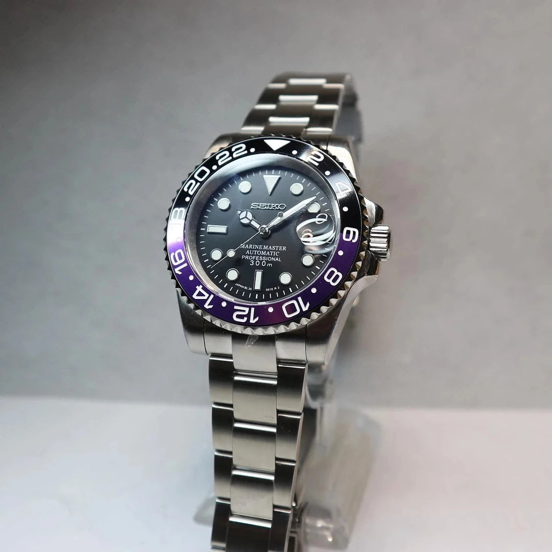 Vorderansicht der Seiko Mod GMT Joker. Automatikuhr mit schwarzem Zifferblatt, violett-schwarzer GMT-Lünette und Edelstahlarmband auf hellem Hintergrund.