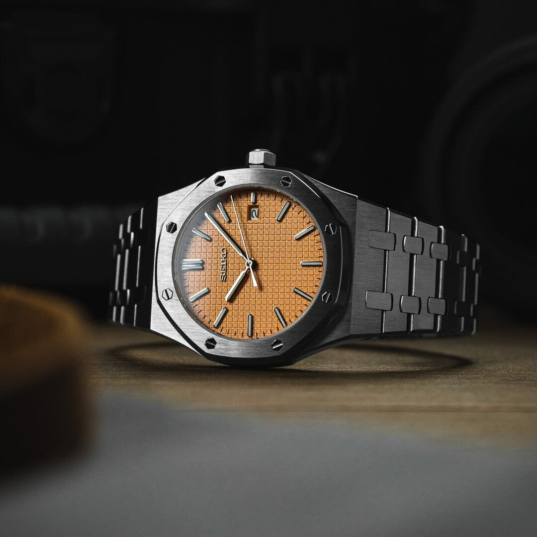 Horizontale Ansicht der Seiko Mod Royal Oak Salmon. Automatikuhr mit strukturiertem lachsfarbenem Zifferblatt und gebürstetem Edelstahlarmband auf Holzoberfläche