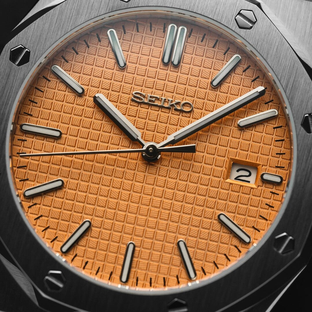 Nahaufnahme des Seiko Mod Royal Oak Salmon Zifferblatts mit lachsfarbenem Waffle-Muster, applizierten Indizes und Datumsanzeige bei 3 Uhr