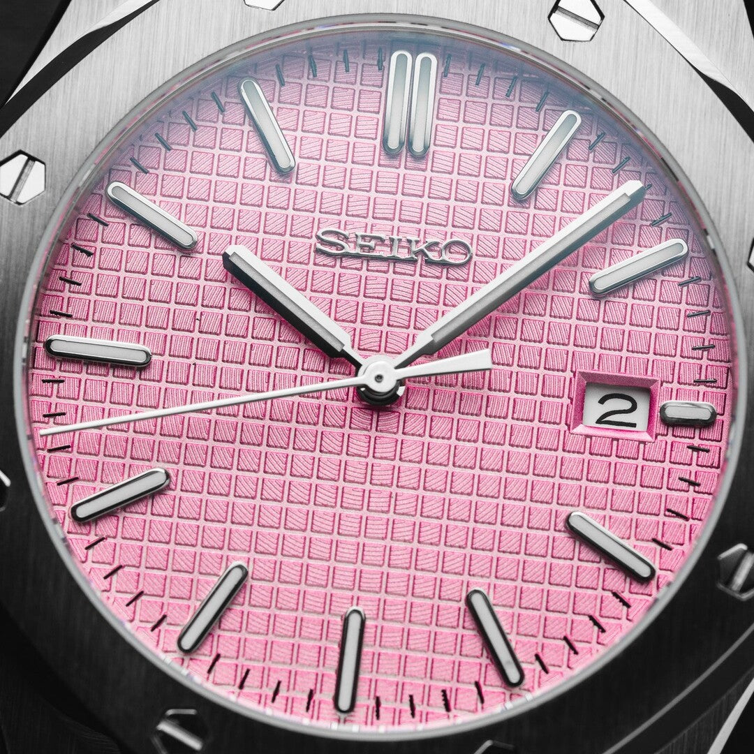 Close up front view of the Seiko Mod Royal Oak with a pink textured dial, silver indices, and polished hands, highlighting the brushed stainless steel case edge and framed date window.