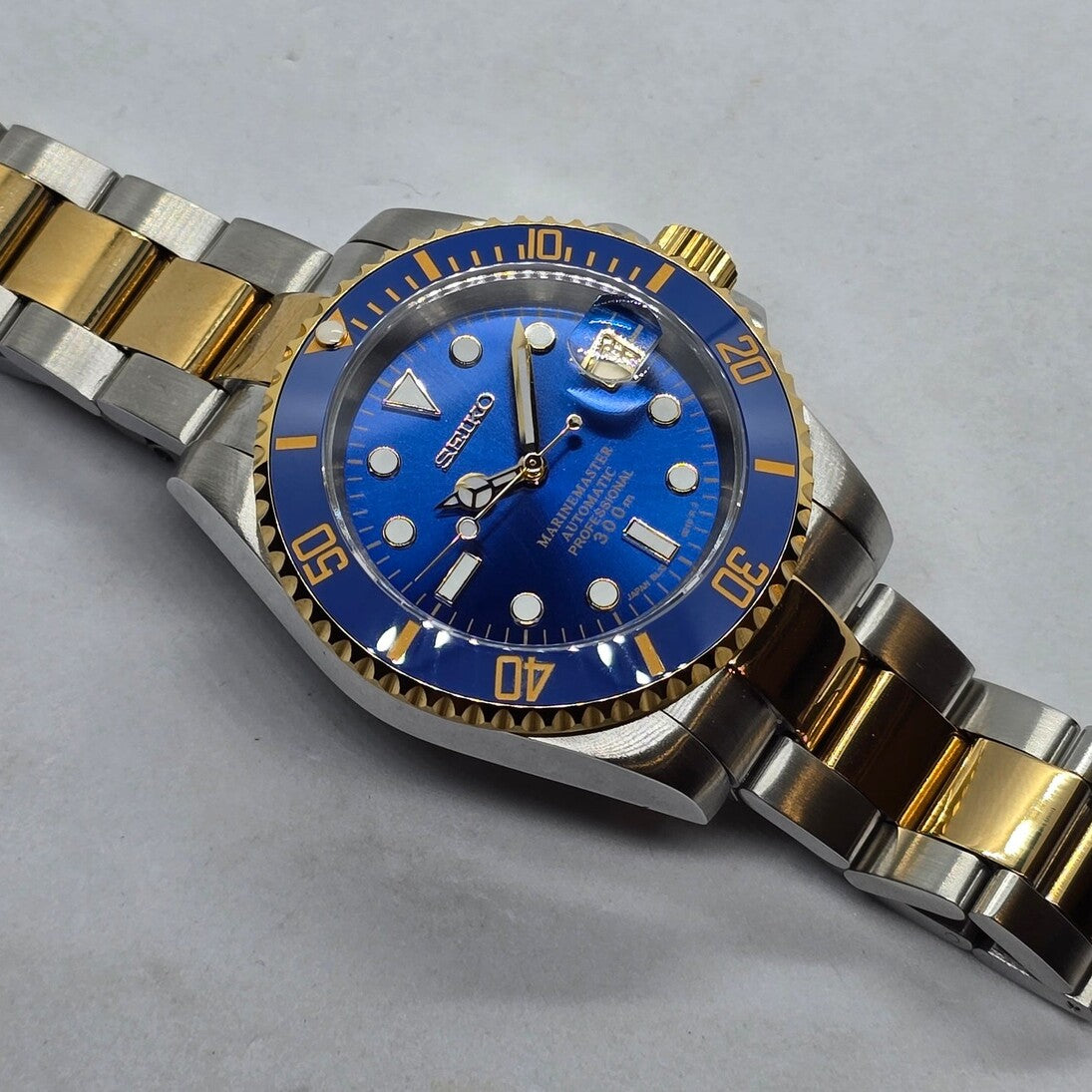 Top angled view Seiko Mod Submariner blue dial gold bezel two tone bracelet on table