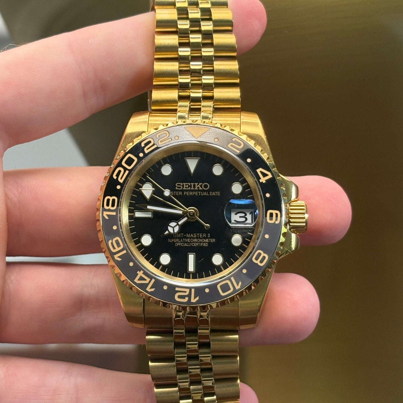 GMT Gold Frontansicht, goldene Keramiklünette, schwarzes Zifferblatt, Leuchtindizes, Jubilee Armband und Dual-Time-Funktion