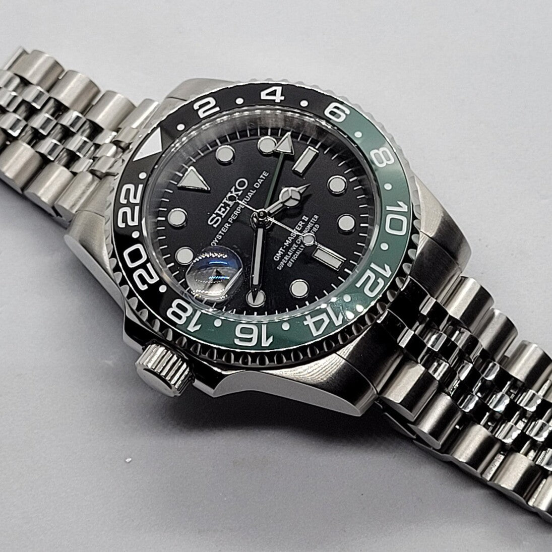 Seiko Mod GMT Sprite Nahaufnahme mit klarem Zifferblatt, gebürstetem Edelstahlgehäuse und schwarz-grüner Lünette
