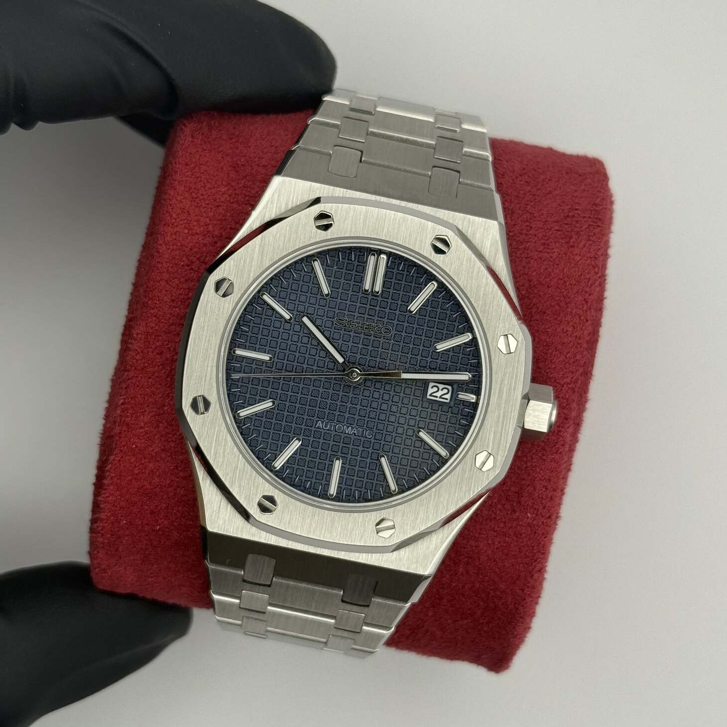 Draufsicht der Seiko Mod Royal Oak Blue mit navyblauem Grid-Zifferblatt, Edelstahlarmband und Datumsanzeige auf rotem Kissen